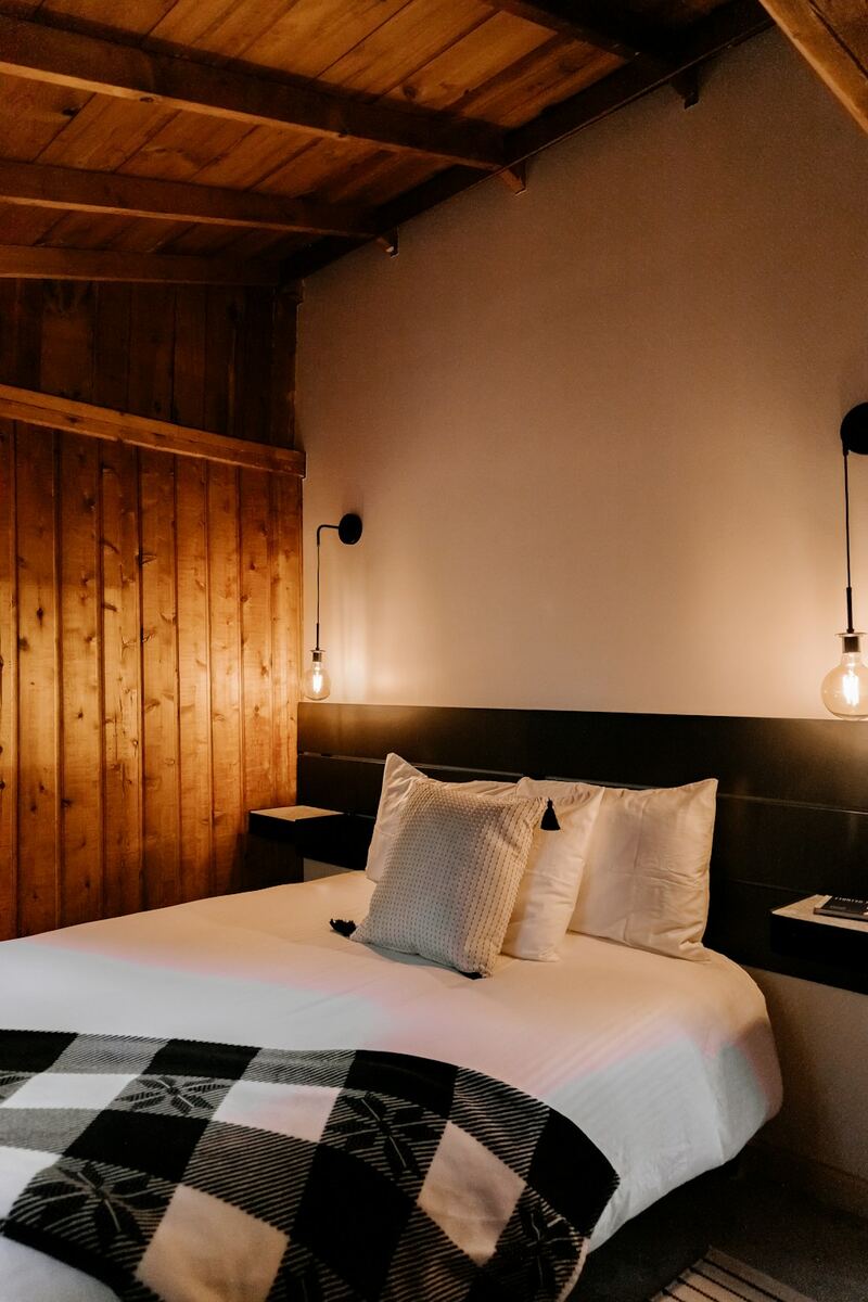 Cama de casal arrumada, com parede de madeira e luminárias de leitura