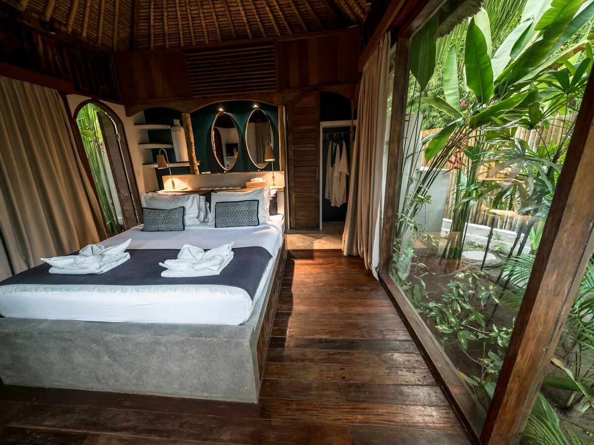 Suíte com cama de casal e parede de vidro voltada para a mata