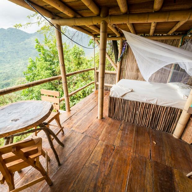 Cama com mosquiteiro em varanda de madeira com vista para as montanhas